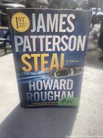 Front cover of the book 'Steal' by James Patterson and Howard Roughan, showing title and author names, with first-time-in-print badge and a small numbered sticker.