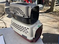 Two pet kennels stacked, a black/grey one on top missing some side clamps, beige/maroon one on bottom intact