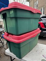 Photo of two large green Rubbermaid totes stacked, showing red lids and signs of wear