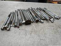 Over 30 metal leather stamps and punch tools laid out on a workbench surface showing variety of textured and patterned heads used for leather crafting.
