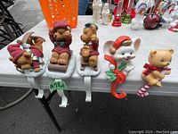 Five Christmas stocking hangers with animal designs displayed on a table among other holiday items.