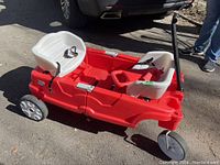 Side view of red folding wagon with two white seats and black handle in need of repair.