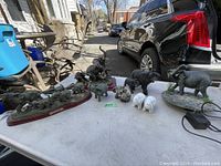 Lot of various elephant figurines including statues, a water fountain, and salt & pepper shakers on a table outdoors.