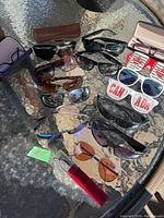 Wide view of assorted sunglasses and eyeglasses on glass table including novelty Canada sunglasses and carrying cases