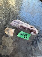 Photo showing two mineral specimens placed on a textured glass surface. One is a purple amethyst cluster; the other is a clear to slightly smoky quartz crystal.