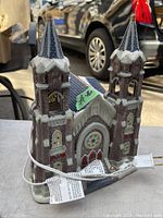 Ceramic Victorian style light-up church with twin steeples, snow on the roofs, stained glass window and lit interior visible through the windows and doors.
