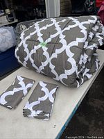 Photo showing folded king size comforter with grey and white geometric pattern along with two matching pillow shams laid beside it.