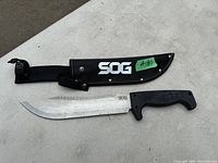 Full view of SOG Jungle Knife with blade and black handle alongside black nylon sheath marked with SOG logo