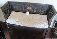 Full view of antique black painted mahogany bench with double wicker caning and beige floral seat cushion.