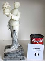 Full front view of white soapstone female figure sculpture with vase, next to a Campbell's soup can and auction card for size reference.