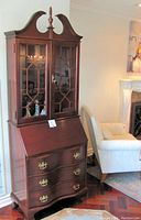 Front view of full Chippendale secretary desk cabinet with bonnet top, glass-front upper cabinet and closed drop-front writing surface.