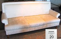 Front view of the cream white sofa showing three seat cushions, rolled arms, and wooden legs on a patterned carpet.