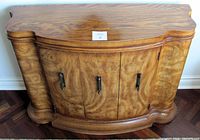 Full front view of the wooden commode showcasing burled veneer with three cabinet doors and metal handles.