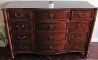 Frontal view of large dresser showing 12 drawers with brass handles and knobs, curved front, and dark polished wood finish.