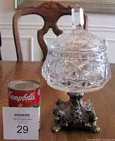 The lidded vintage lead crystal compote with detailed pinwheel cuts on an ornate brass footed base shown next to a can of Campbell's soup for scale.