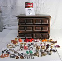 Photo showing 37 pairs of assorted earrings laid out in front of a dark brown wooden jewelry box with six drawers.