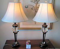 Front view of both lamps with shades illuminated on wooden table in front of botanical artwork
