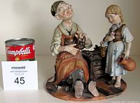 Front view of figurine showing shoemaker seated with tools and standing young girl.
