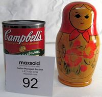Photo of largest Russian nesting doll next to Campbell's soup can for size reference, showing the doll at about 5 inches tall and with a red headscarf and floral design on body, with auction inventory card in front.