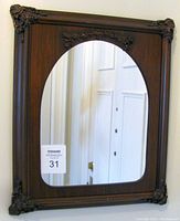 Vintage wall mirror in a dark wooden frame with bronze decorative accents at four corners and arch-shaped mirror glass.