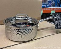 Front angled view of the Cuisinart 1.5 QT saucepan with lid, showing the hammered stainless steel body and attached handle, placed on a cardboard surface.