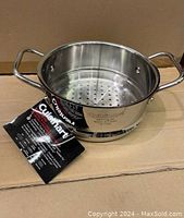 Front angle of the Cuisinart universal steamer insert showing dual handles, perforated base, and attached branded hang tag.