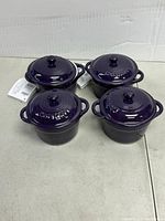 Four purple mini stoneware casseroles with matching lids, top view showing handles and knob details.