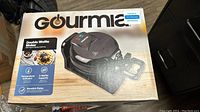 Box of Gourmia Double Waffle Maker with clear text about features and condition approval label