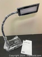 Black Trotronics TT-DL11 LED desk lamp wrapped in plastic, showing flexible gooseneck and lamp head with protective covering, with product manual beside it.