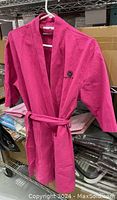 Full view of pink waffle weave Meredith Marks robe hanging on white hanger with logo visible on chest, showing 3/4 sleeves, belt tied at waist, and two front patch pockets.