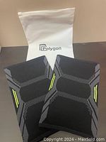 Pair of new Polygon knee compression sleeves laid flat on a surface with white Polygon branded packaging in the background.