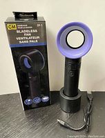 Photo of the front view of the purple-ringed bladeless fan standing upright with box and charging cable.