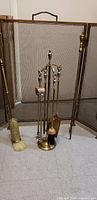Front view of antique bronze fireplace tool set including broom, shovel, tongs, poker on a stand, with mesh screen in background