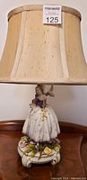Front view of the antique porcelain figurine lamp with lampshade, showing a woman in a white dress with yellow floral details and purple bodice