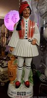 Front angled view of the porcelain statue depicting a man in traditional Greek clothing with ouzo bottle at side