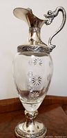 Full front view of the ewer showing the clear glass with raised floral bubbles and silver dragon handle.