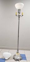Full view of the standing silver plated floor lamp with milky white glass shade on top and additional milk glass shade on floor beside it.