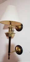 Side view of first wall sconce lamp showing brass components, wooden arm, round mounting base, and fabric lampshade.