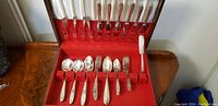 Full view of the 44-piece silver cutlery set inside red felt-lined wooden box showing knives, forks, spoons and other utensils arranged in slots.
