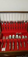 Full set inside wooden box showing arrangement of forks and spoons with red fabric lining