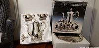 Complete 5-piece silver coffee set in original white styrofoam packaging alongside original box showing completed set on a matching tray.
