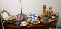 Full view of lot including porcelain plates, cat figurines, and silver items arranged on table.