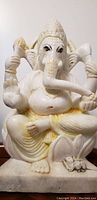 Frontal close-up showing detailed face and upper body of the white marble Ganesha statue with painted eyes and trunk raised.