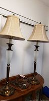 Pair of vintage table lamps standing on a wooden surface, showing overall design with beige fabric shades, brass bases, and textured white glass midsections.