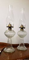 Full view of both vintage glass oil lamps standing side by side on a wooden surface.