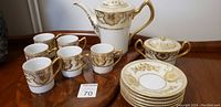 Overview of coffee pot, sugar bowl, cups, and saucers showing gold hand painted decoration and set arrangement