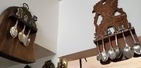 Two wooden hanging frames displaying antique British souvenir silver spoons, mounted on the wall, showcasing layout and style of the lot