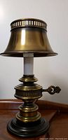 Side view of vintage golden lamp showing the polished brass body, decorative key-shaped handle, and golden lampshade with ventilated top edge.