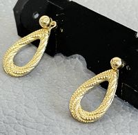 Front angle close-up of both earrings mounted on black display card showing the teardrop textured design and round ball stud in yellow gold.