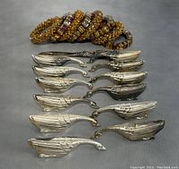 Set showing 12 silver plated swan knife rests laid out in rows on a surface with 8 decorated napkin rings stacked behind them.